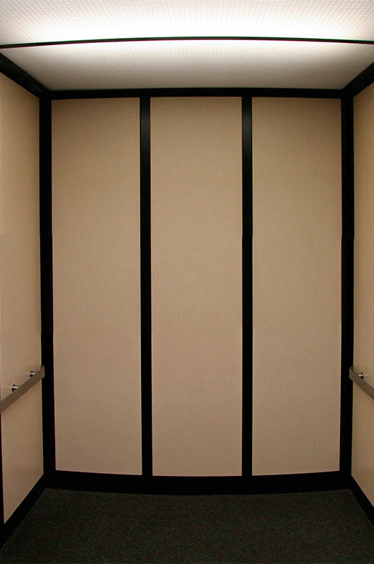 The inside of an empty elevator at a doctors office. The elevator is bland, beige in color with flourescent lighting.