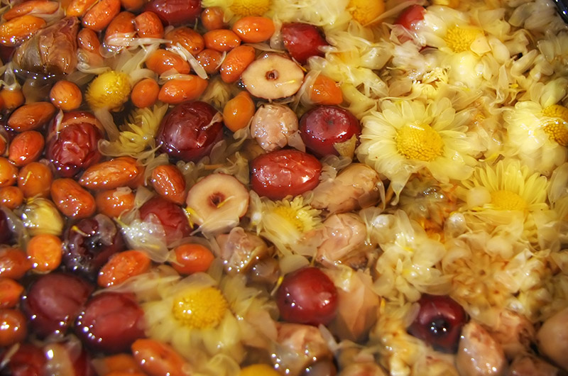 Slow cooking jujubees, goji berries, rose buds, and chrysanthemum flowers for a tea base