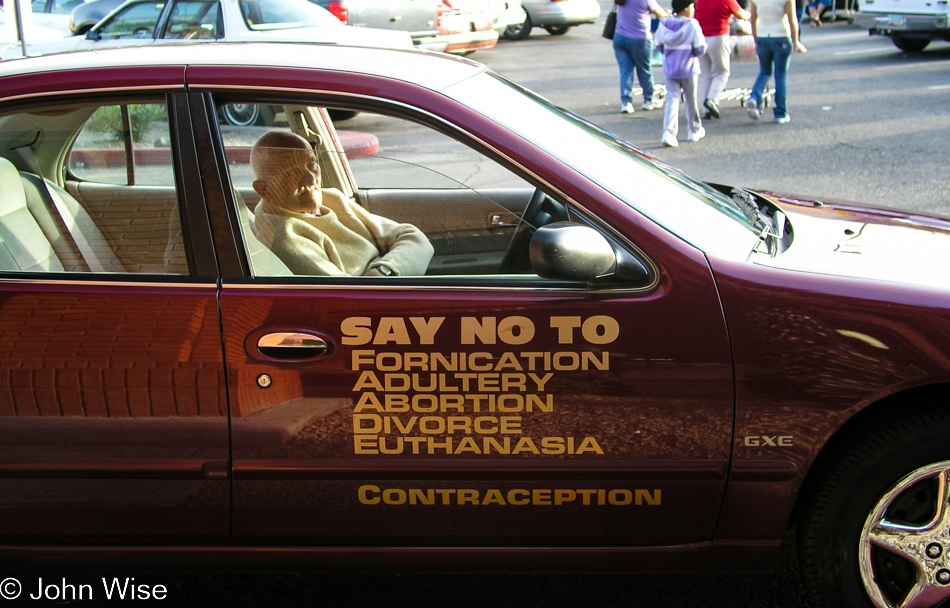 Old guy sitting in his car with sign on door saying, 'Say No To: fornication, adultery, abortion, divorce, euthanasia, contraception' 