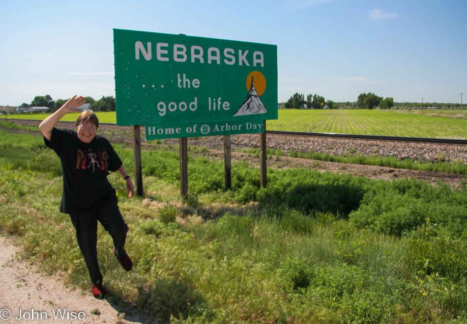 In front of the Welcome to Nebraska State sign celebrating the Good Life with Jutta Engelhardt
