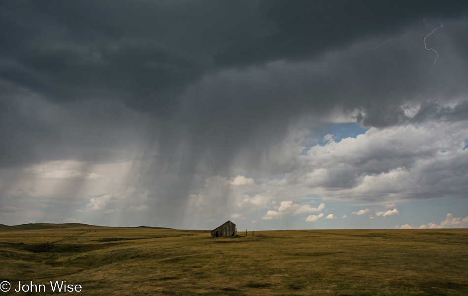 A band of rain and a whisp of lightening hover over the flattening landscape of the Great Plains in northeast New Mexico