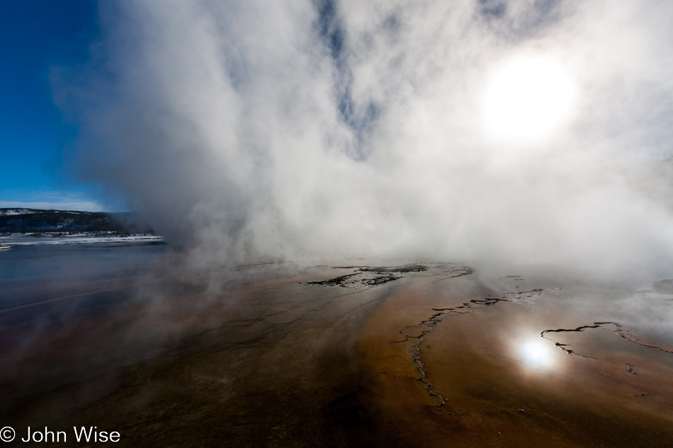 Near the edge of the steam obscured Grand Prismatic Spring with brown and red thermophilic mat in the foreground on the Midway Geyser Basin in Yellowstone National Park January 2010 