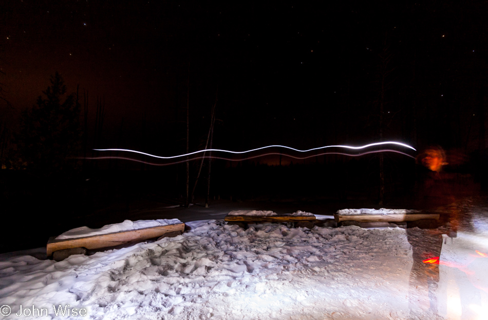 Long exposure at night of someone walking through the photo with a head mounted flashlight with a ghostly image of Caroline Wise on the right at Fountain Paint Pots in Yellowstone National Park January 2010