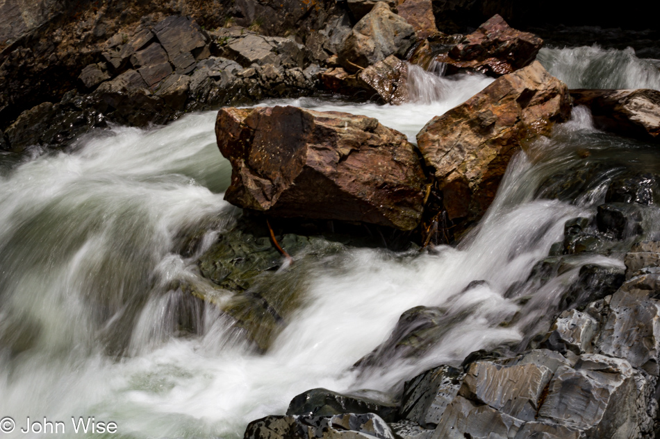 A cascade that flows under the road through a natural hole in the rock is seen here where it emerged just a few feet above this photo