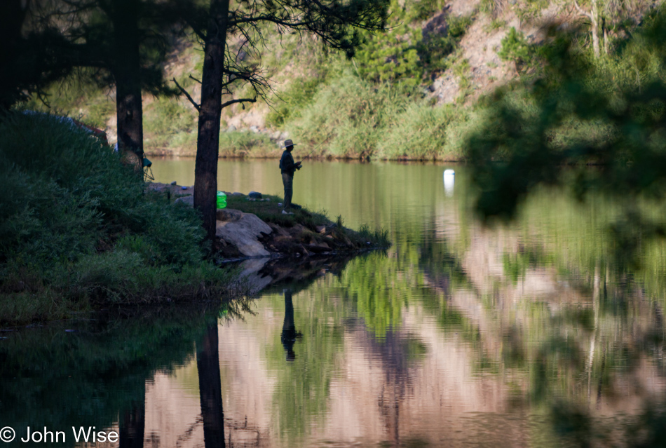 A man fishing next to the reflective waters of Vallecito Reservoir near where the waters of the Los Pinos River enter the reservoir
