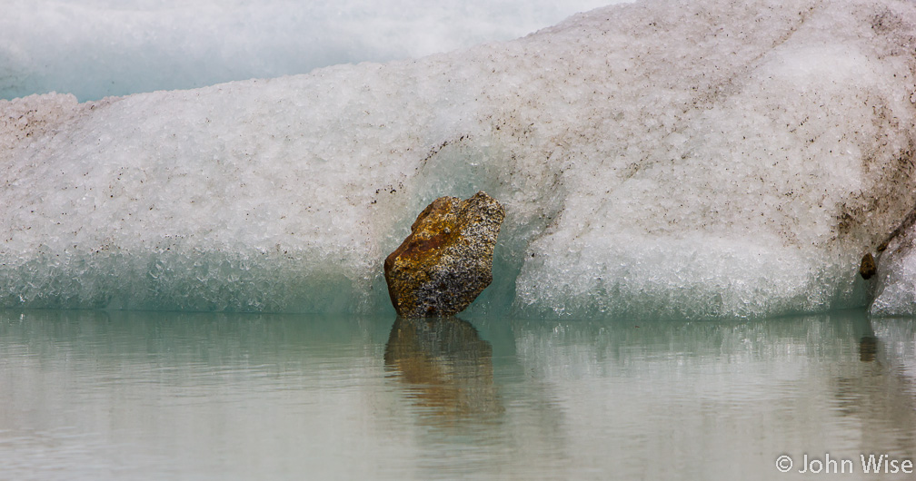 A rock clings to the edge of an iceberg as it floats away from the glacier and towards the Pacific Ocean in Alaska