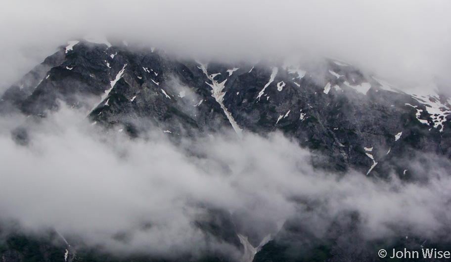 Mountain side peaking out between low clouds along the Alsek River in British Columbia, Canada