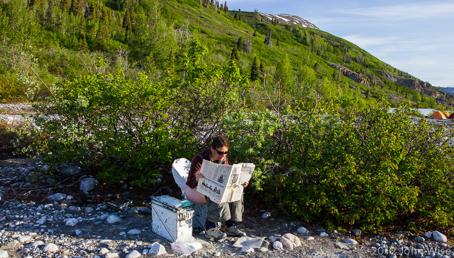 Caroline Wise reading the paper early in the morning while taking care of business in Kluane National Park Yukon, Canada