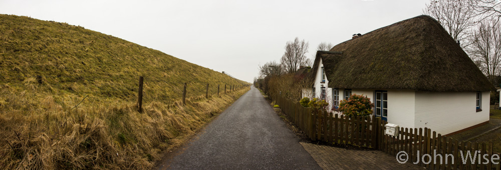 On a narrow road separating some homes from the sea behind the dike on the left. In northwest Germany.