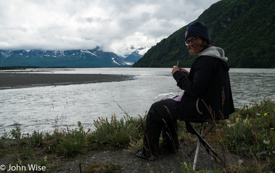 Caroline Wise knitting next to the confluence of the Tatshenshini and Alsek Rivers in British Columbia, Canada