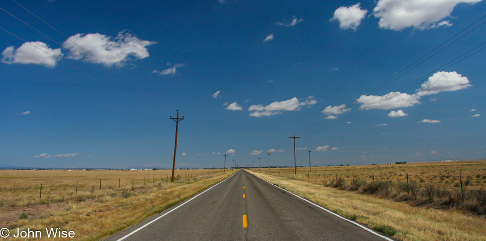 South of Estancia, New Mexico on highway 41 looking down a flat long road under blue skies with little fluffy clouds
